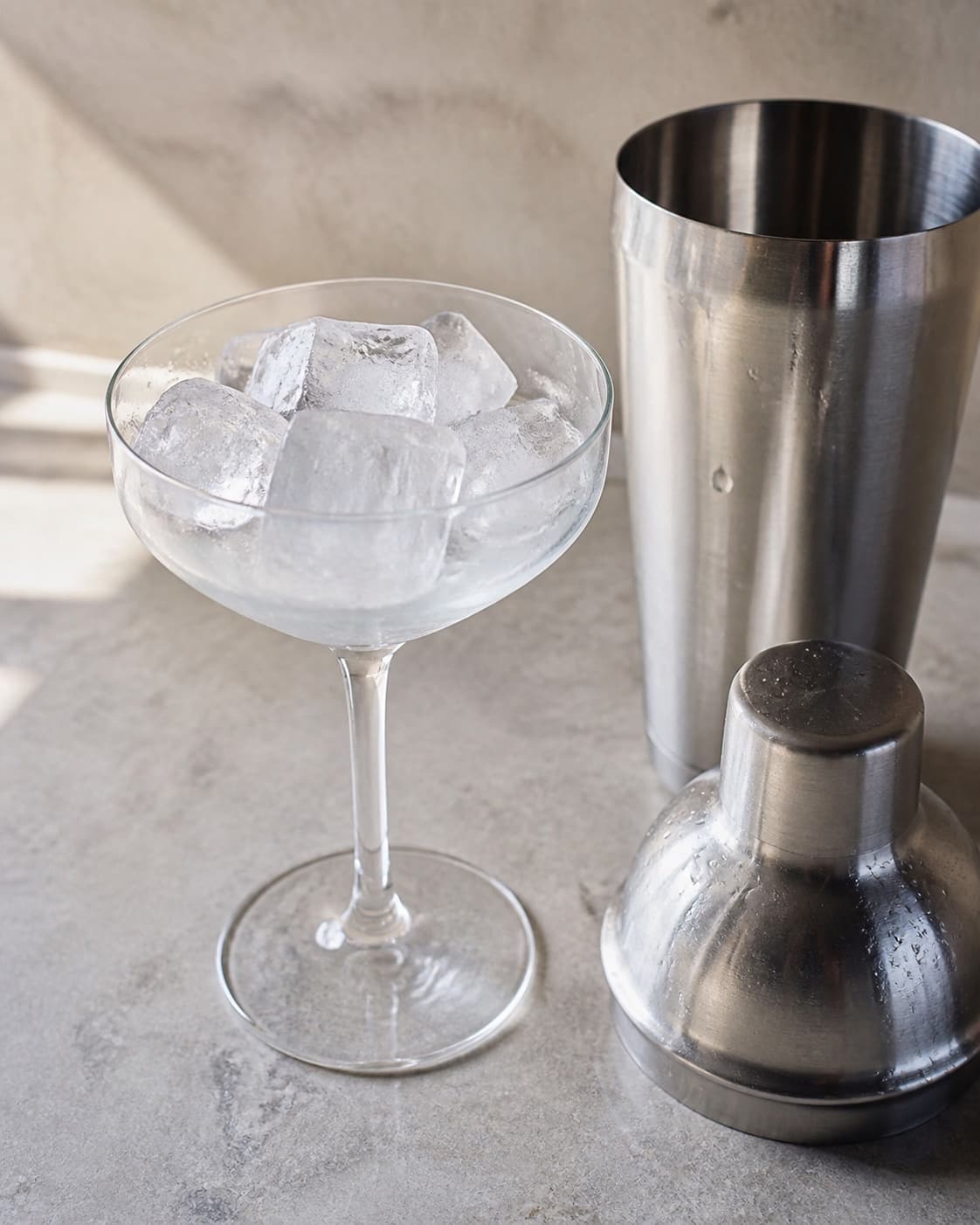 To coupeglas fyldt med is ved siden af en åben cocktailshaker