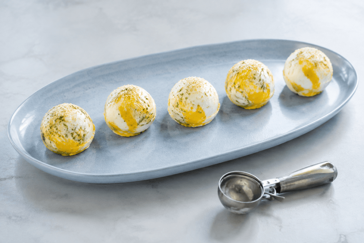 Fem kugler mango-lime-yoghurtis med ristet kokos på et lyseblåt fad