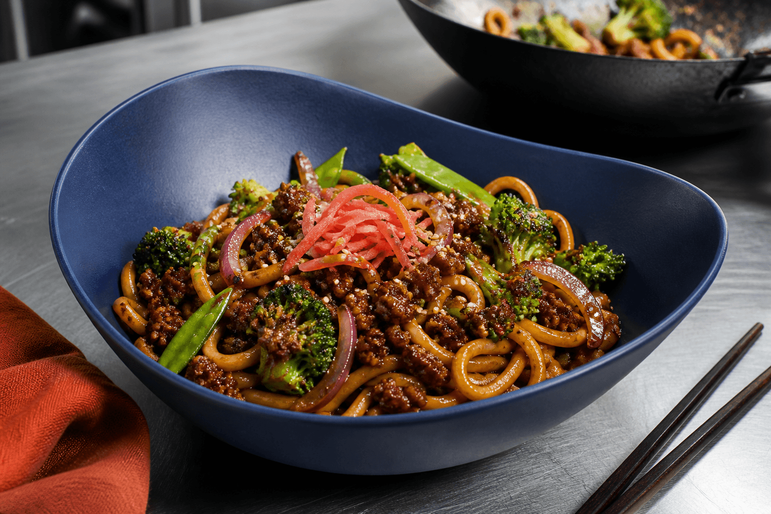Teriyaki-wok med udonnudler, sprødstegt hakket oksekød, broccoli, sukkerærter og syltet ingefær i koboltblå skål