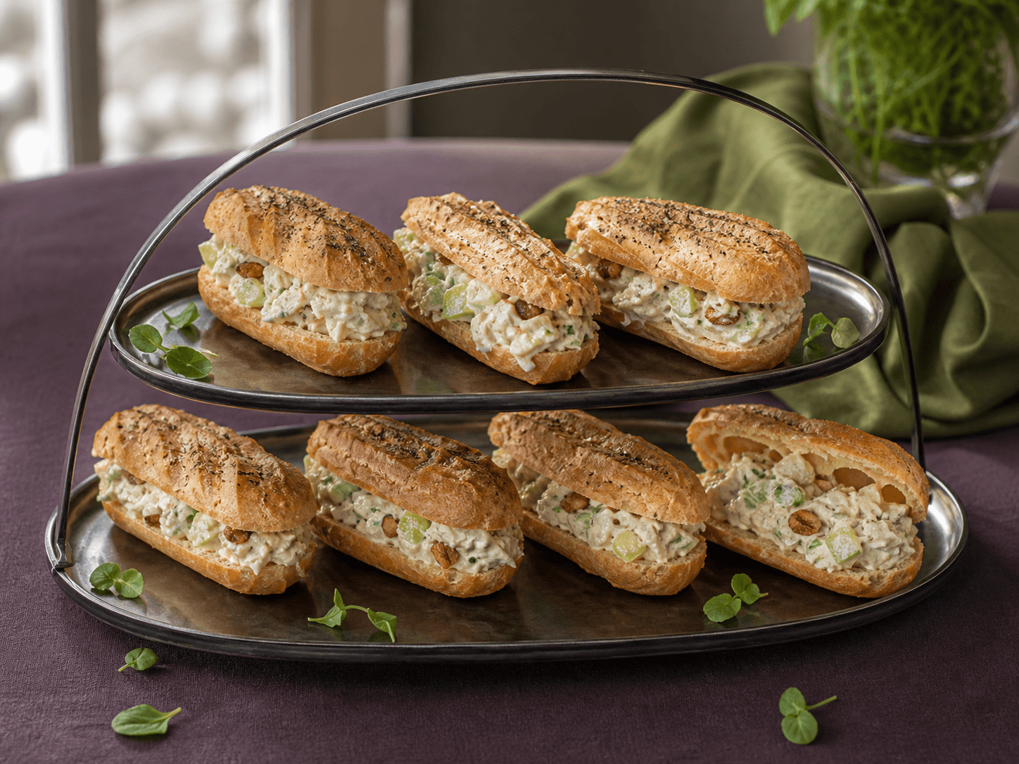 Otte små aflange vandbakkelses-eclairs fyldt med cremet kyllingesalat, grønne æbletern, selleri, hasselnød og estragon på mørkt sølvfad