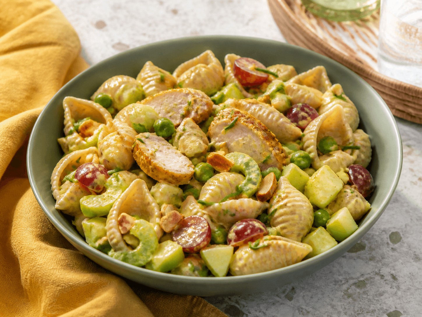 Kold fuldkornsskalpastasalat med gylden kylling, æble, selleri, ærter, røde druer, mandler og let mango-karrydressing i salviegrøn skål