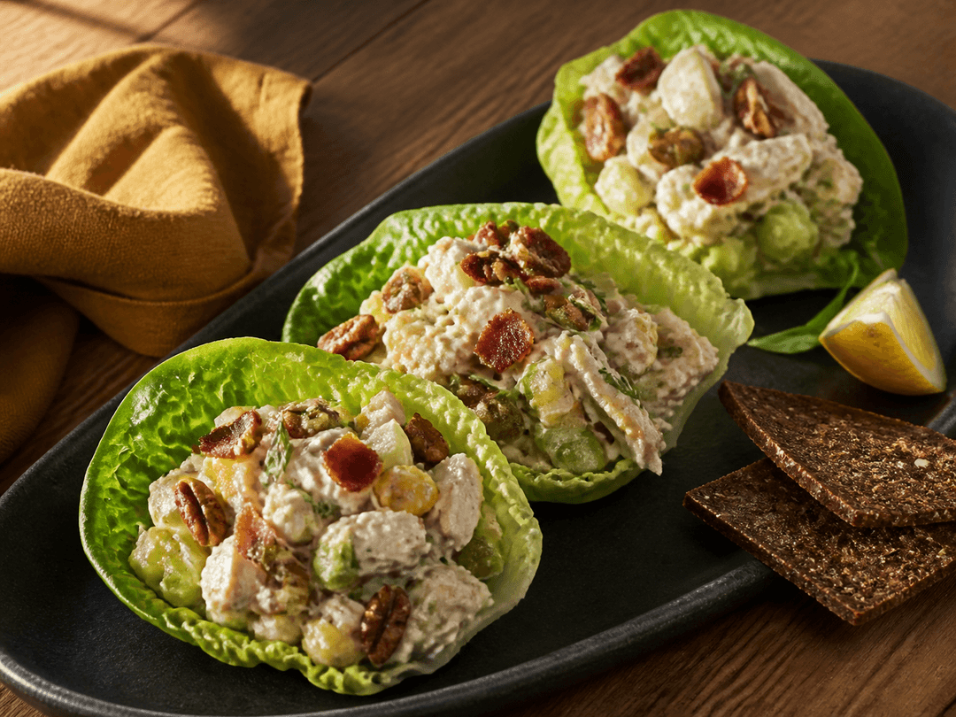 Tre hjertesalatblade fyldt med cremet kyllingesalat med sprød bacon, grønne æbletern, selleri, cornichoner, pekannødder og estragon på koksgråt fad