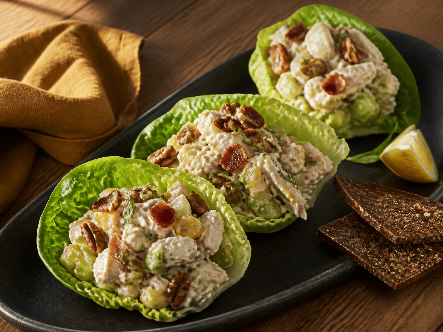 Tre hjertesalatblade fyldt med cremet kyllingesalat med sprød bacon, grønne æbletern, selleri, cornichoner, pekannødder og estragon på koksgråt fad