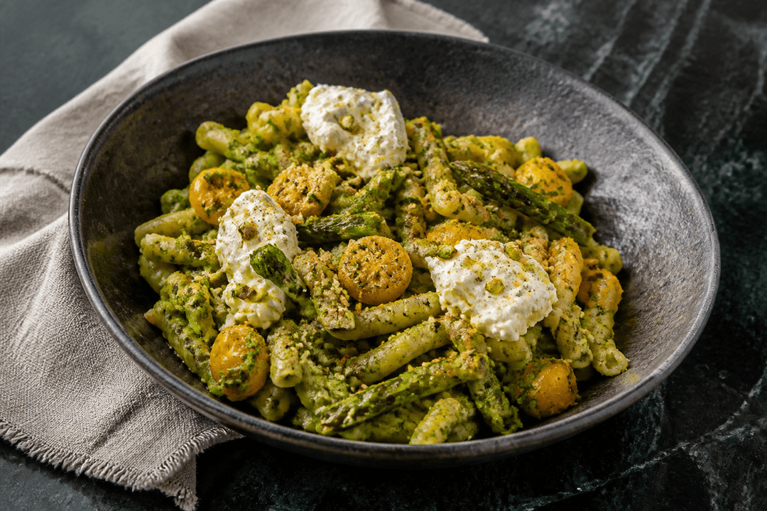 Koksgrå skål med casarecce i broccoli-pistaciepesto, grillede asparges, gule tomater, stracciatella og citronkrumme