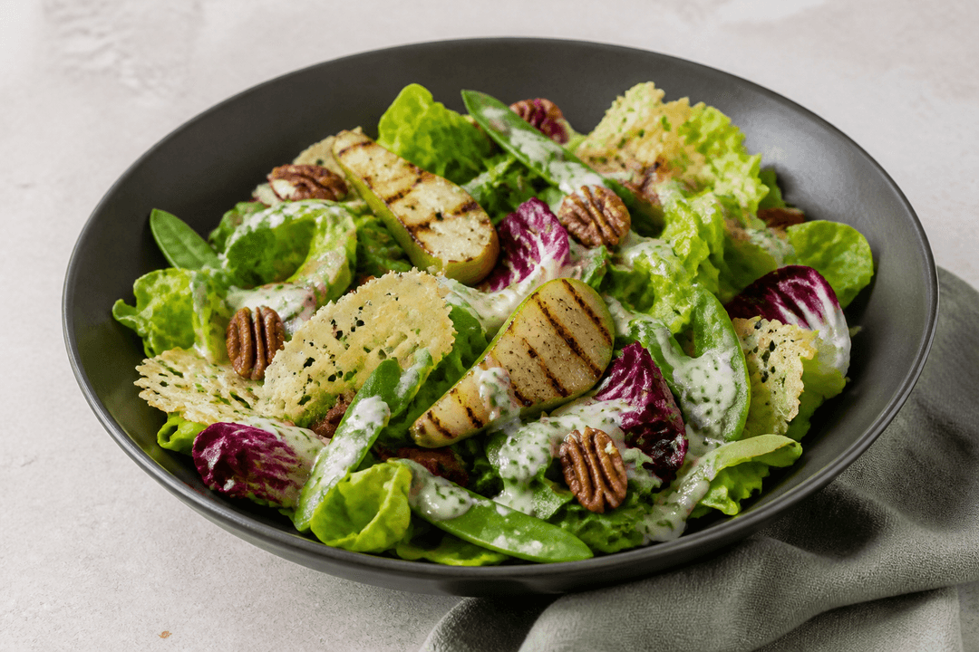 Koksgrå skål med grøn salat, grillede pærebåde, radicchio, selleri, sukkerærter, parmesanflager, pekannød og parmesan-kærnemælksdressing