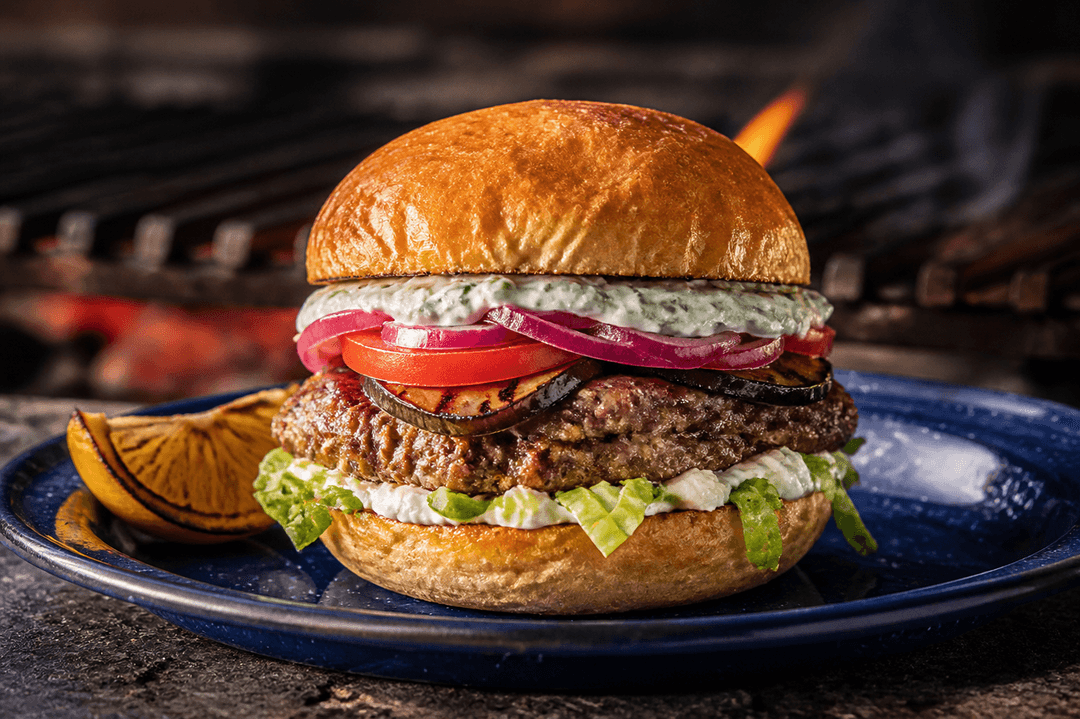 Græsk lammeburger i ristet kartoffelbolle med to tynde bøffer, feta, grillet aubergine, mynte-tzatziki, tomat, salat og syltet rødløg