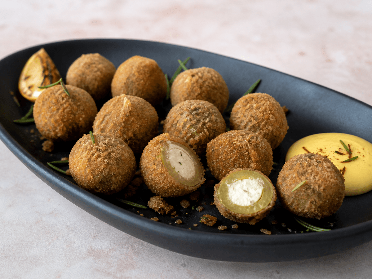 Langt sort fad med rugpanerede friterede grønne oliven, to åbne med citron-gedeostkerne, safranaioli, rosmarin og grillet citron