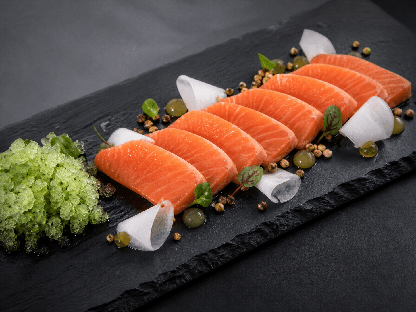 Lang mørk skifer med otte tykke skiver laksesashimi, grøn agurk-shisogranita, syltet daikon, yuzu-tamarigel og ristet boghvede