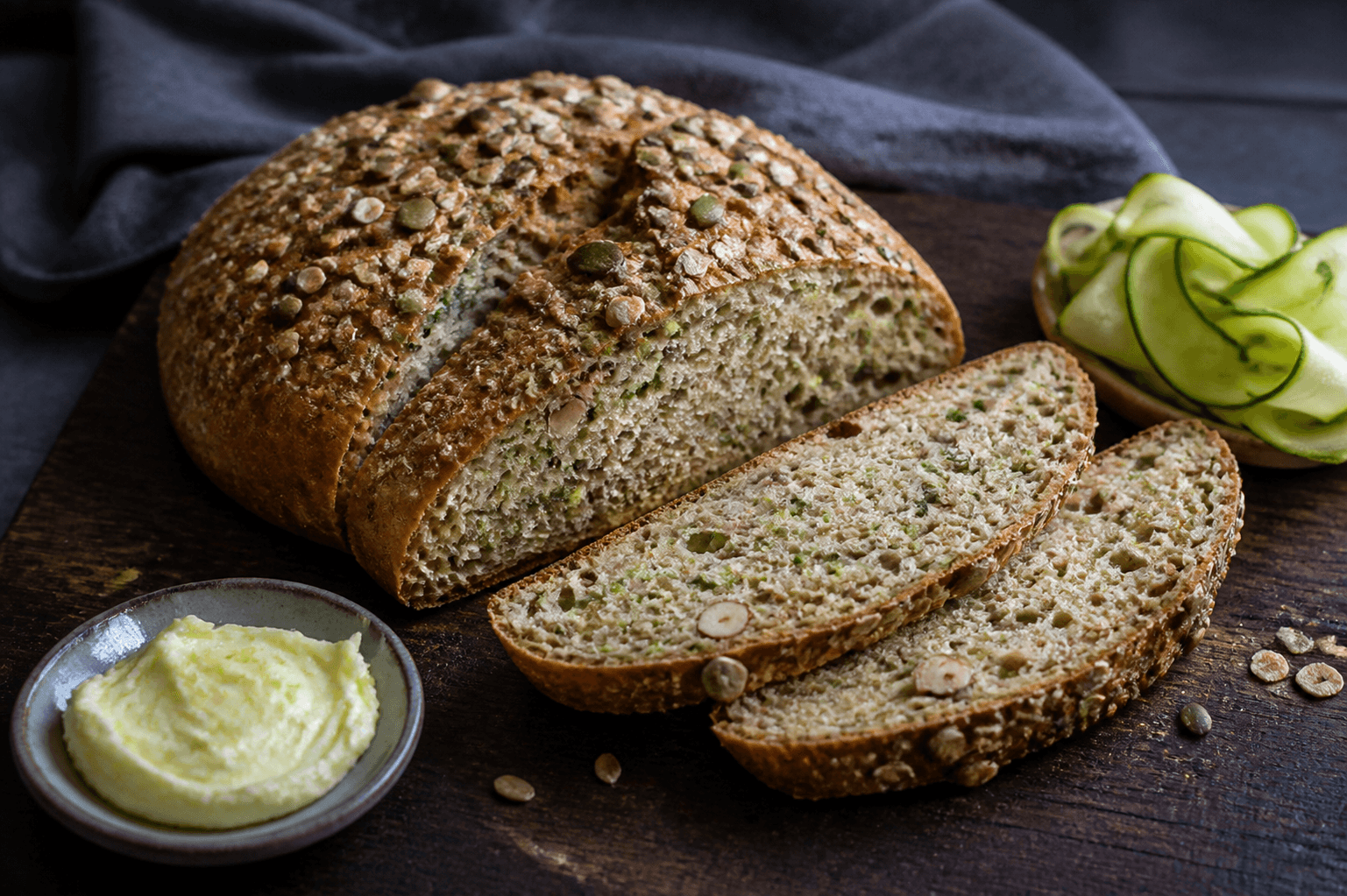 Fritstående ovalt squashbrød med gylden frø- og havreskorpe, to skrå skiver med grøn squash, dild og hasselnød samt citronsmør