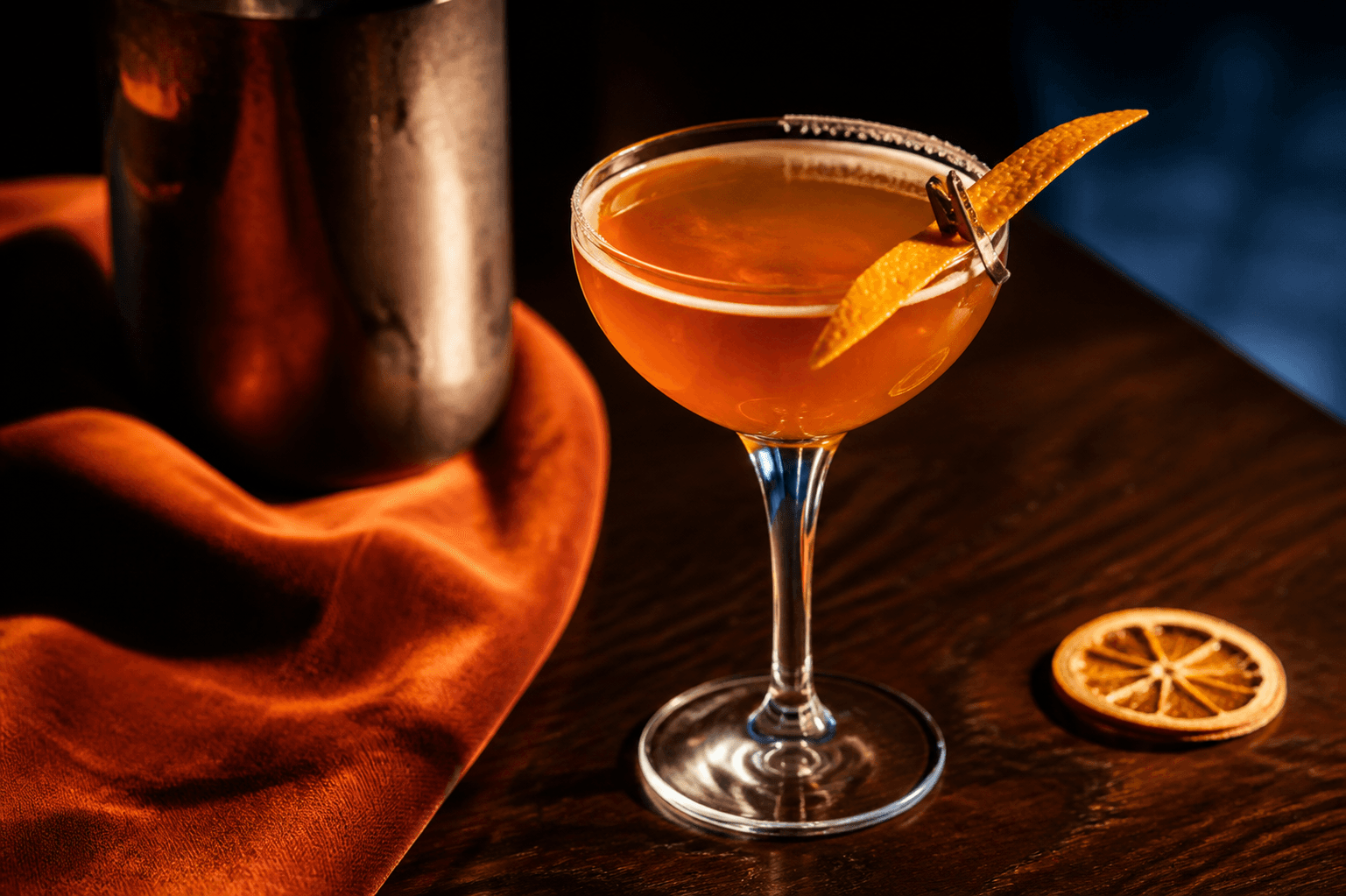 Lille Nick og Nora-glas med klar ravfarvet Sidecar, halv appelsinsukkerkant og lang appelsintwist på mørk valnøddebar med shaker