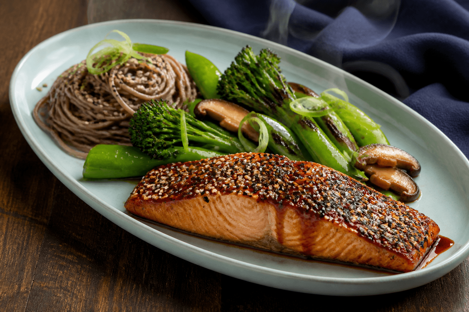 Langt celadongrønt fad med gennemtilberedt miso-teriyaki-laks, sobanudler, grillet broccolini, shiitake, sukkerærter, sesam og forårsløg