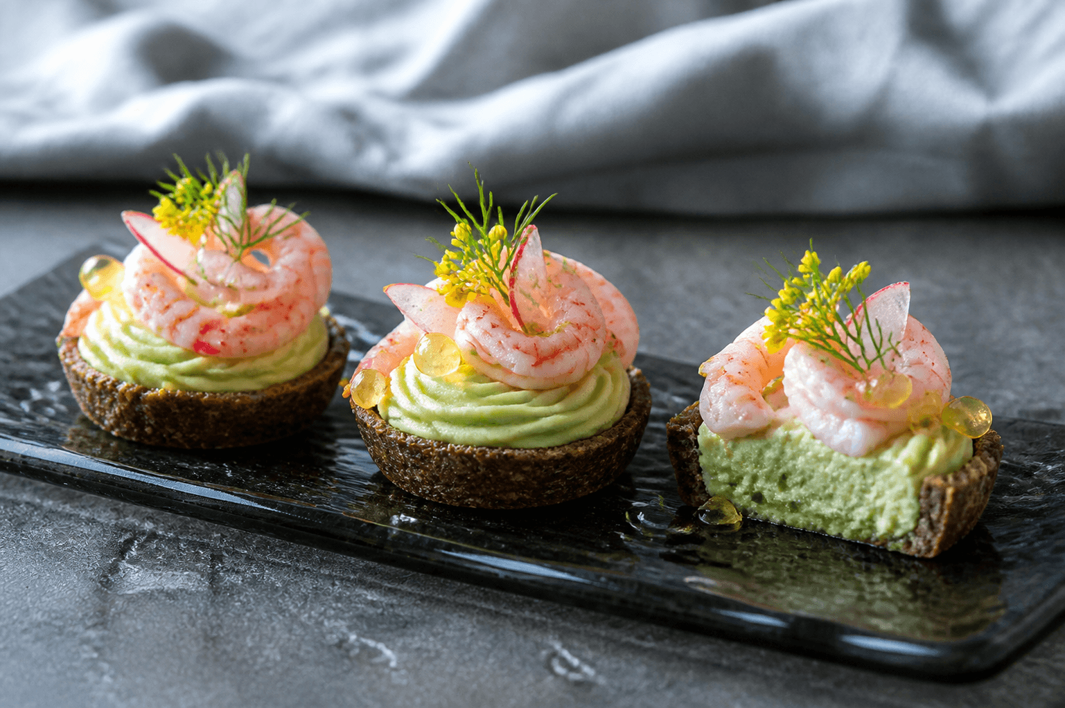 Langt røget glasfad med tre mørke rugtarteletter, avocado-agurkemosse, fuldt tilberedte pink rejer, radise, citrongeléperler og dild
