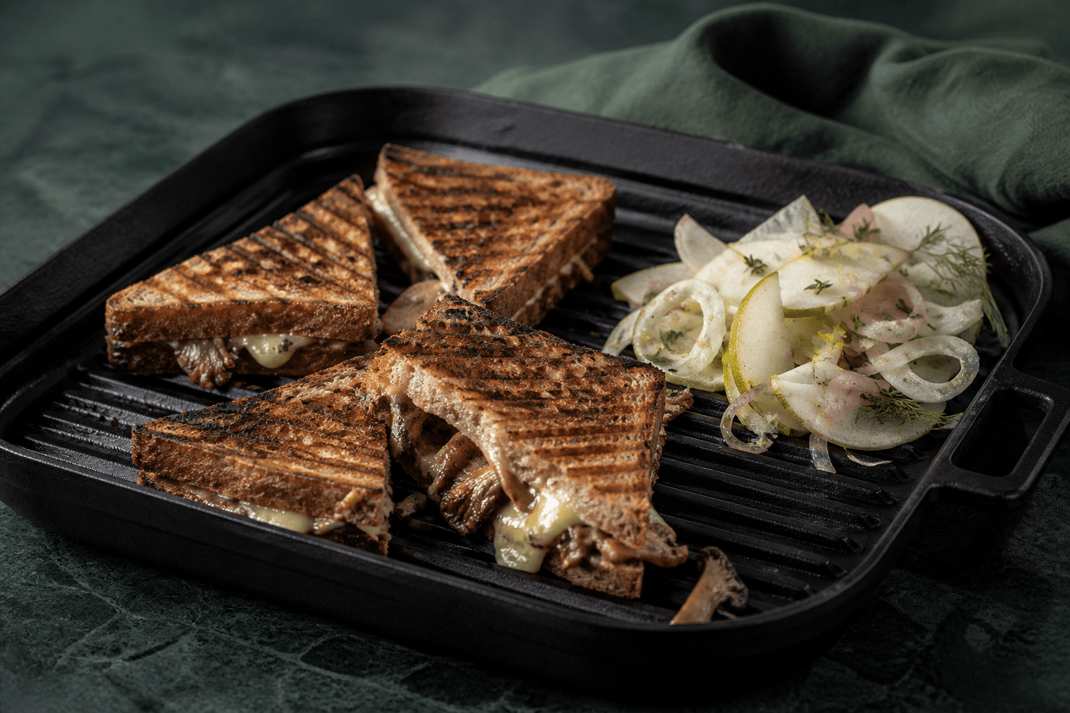 Sort rillet grillpande med fire mørke surdejstoasttrekanter fyldt med gennemstegte svampe, gruyère og trøffelcreme samt pære-fennikelsalat