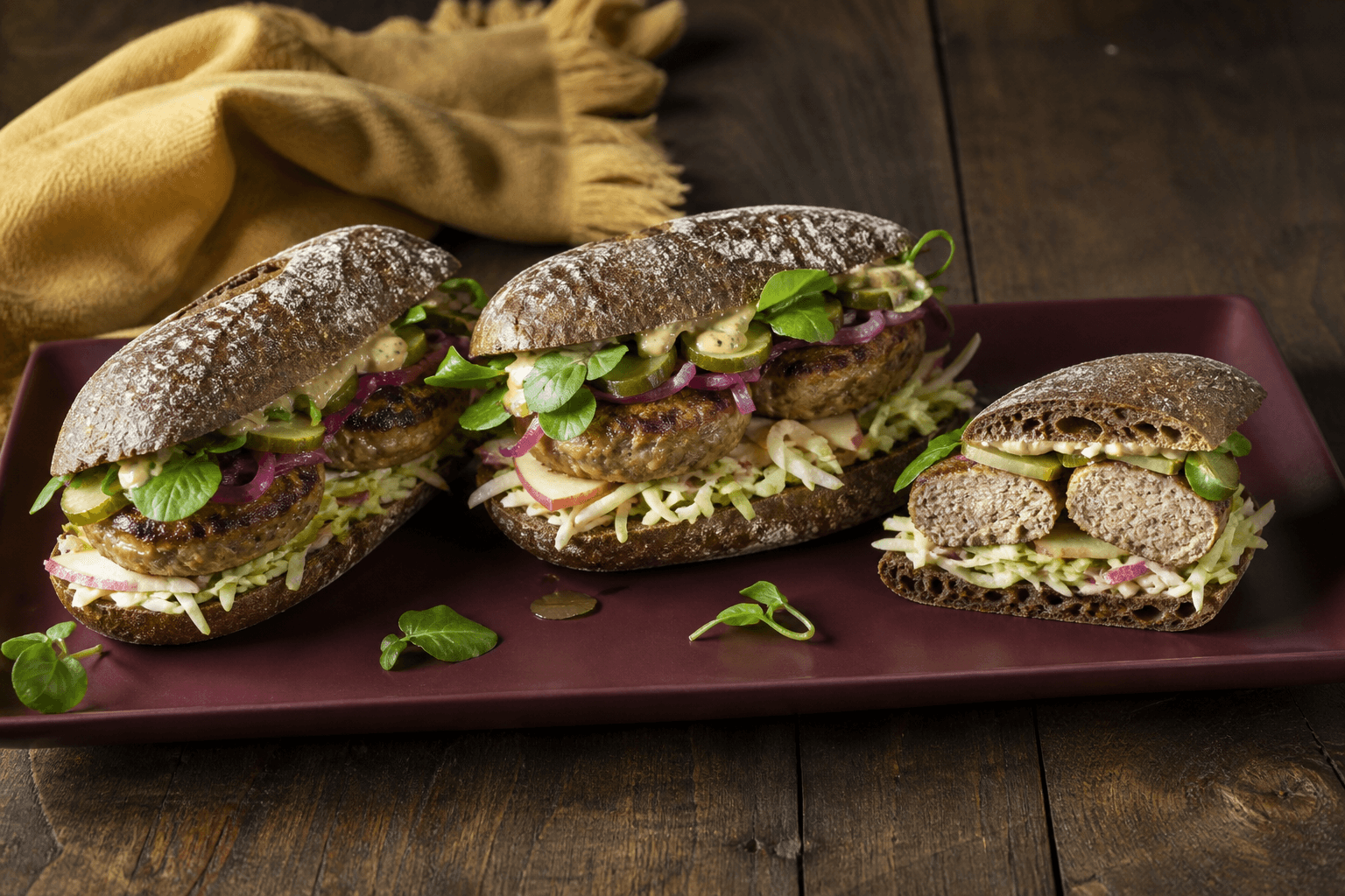 Tre mørke surdejssandwich med fuldt gennemstegte skiver af kalv-flæsk-frikadeller, æble-kålslaw, syltet rødløg, pickles og sennepsremoulade