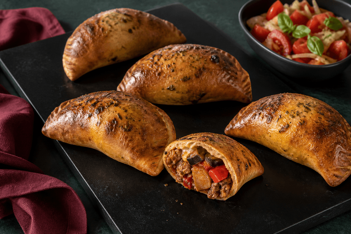 Sort bagestål med fem små mørkgyldne calzone, én åben med fuldt gennemstegt oksekød, aubergine, rød peber, tomat og røget mozzarella