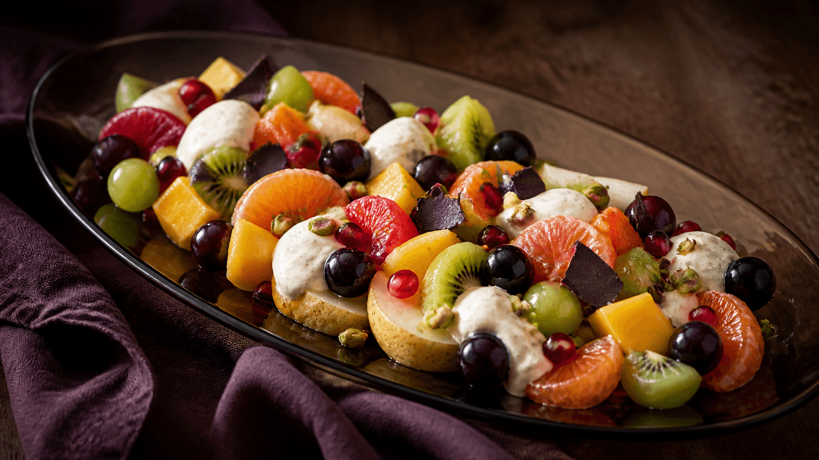 Røgfarvet glasfad med citrus, pære, druer, kiwi, mango og granatæble mellem kold vanilje-råcreme, mørk chokolade og pistacie