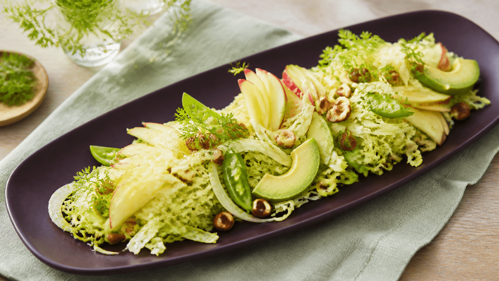 Langt mørkt blommefad med luftig spidskålssalat, røde æblevifter, avocado, høvlet fennikel, sukkerærter, ristede hasselnødder og kørvel