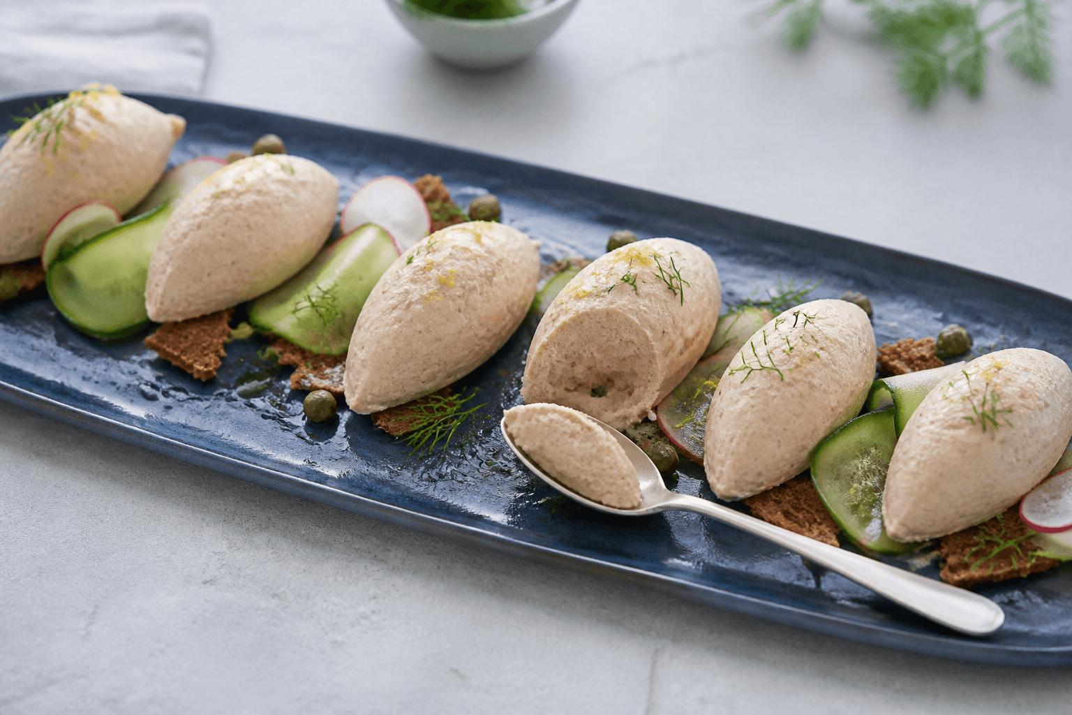 Langt midnatsblåt koldt fad med seks formfaste tunmoussequeneller, rugcrostini, agurk, radise, kapers, citron og dild