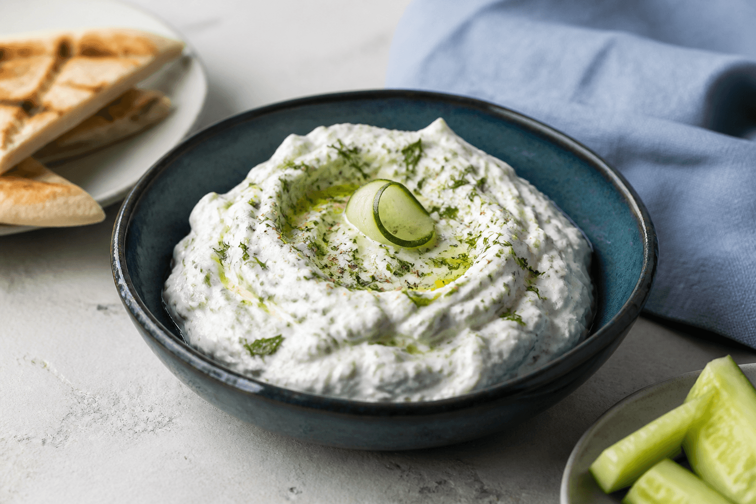 Mørk teal skål med tyk tzatziki, tydelige ske-riller, agurk, dild, mynte, citron, peber og olivenolie