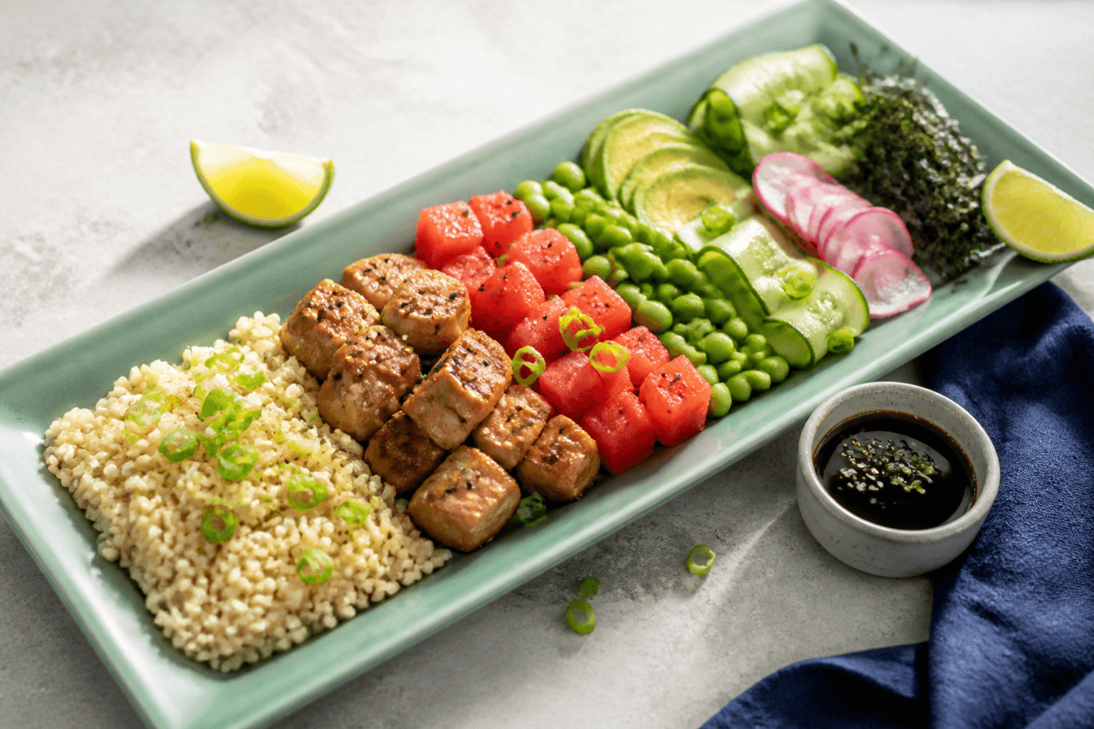 Langt havgrønt poke-fad med brune ris, helt gennemtilberedte brunede tuntern, kold vandmelon, edamame, avocado, agurk, radise og nori