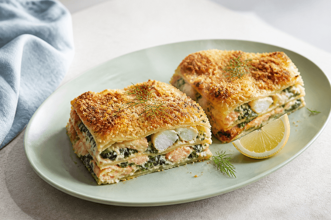 To skårne stykker fiskelasagne med laks, hvid fisk, spinat, citronbechamel og sprød rasp på lysegrønt fad