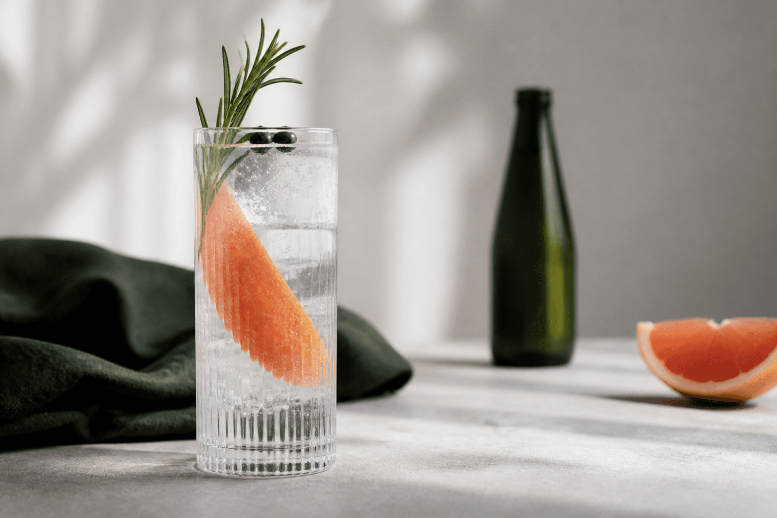 Klar gin og tonic i højt riflet glas med grapefrugtskal, rosmarin, enebær og store isterninger