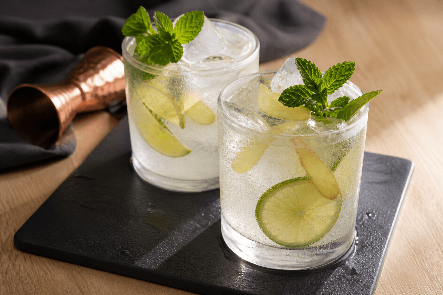 To klare Moscow Mule-drinks i lave glas med lime, frisk ingefær, mynte, is og kobberjigger