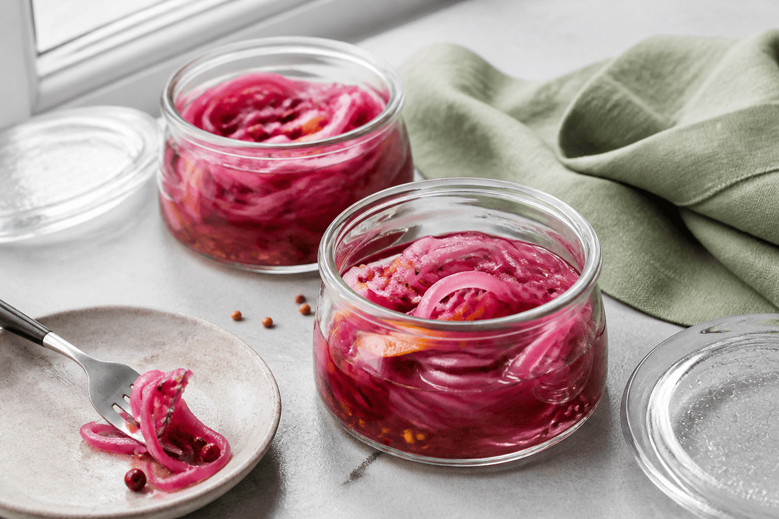 To lave glas med pink syltede rødløg, appelsinskal og krydderier ved lille sandfarvet tallerken
