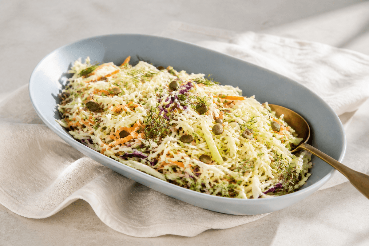 Sprød coleslaw med lys og lilla kål, gulerod, grønt æble, fennikel, dild og græskarkerner på langt lyseblåt fad