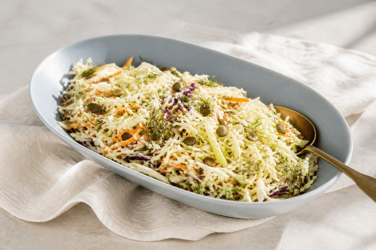 Sprød coleslaw med lys og lilla kål, gulerod, grønt æble, fennikel, dild og græskarkerner på langt lyseblåt fad