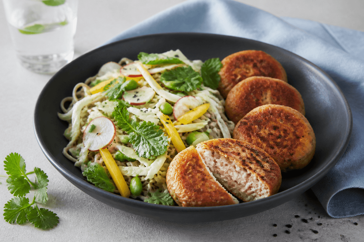 Sobasalat med kål, mango, edamame, radise og fire gyldne laks-torskefiskekager i mat sort skål