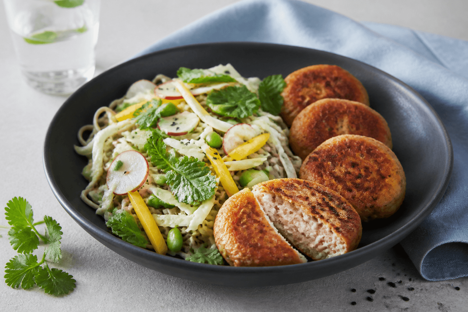 Sobasalat med kål, mango, edamame, radise og fire gyldne laks-torskefiskekager i mat sort skål
