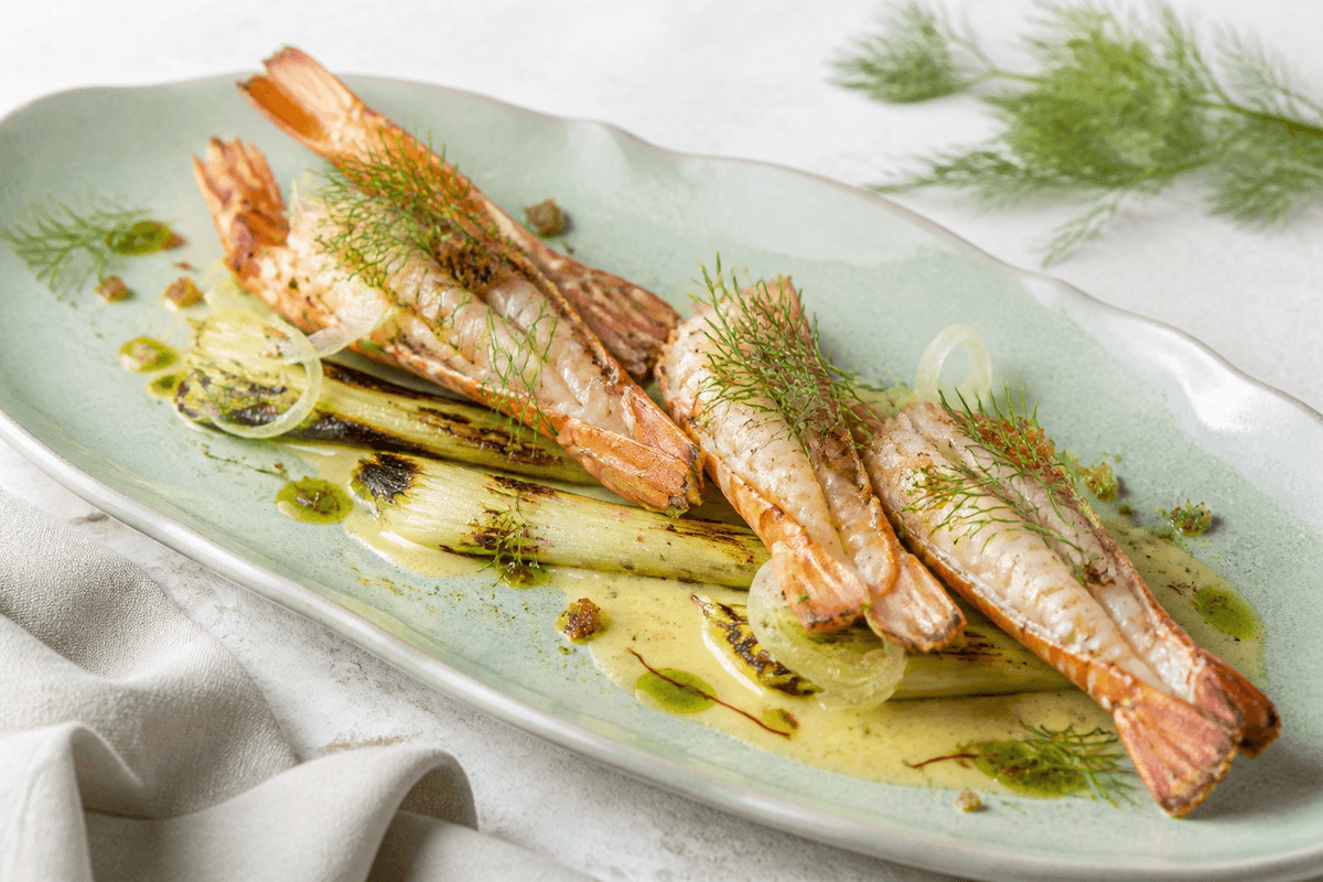 Smørgrillede jomfruhummerhaler med safran-beurre blanc, grillede små porrer, syltet fennikel, dildolie og rugknas på havgrønt fad