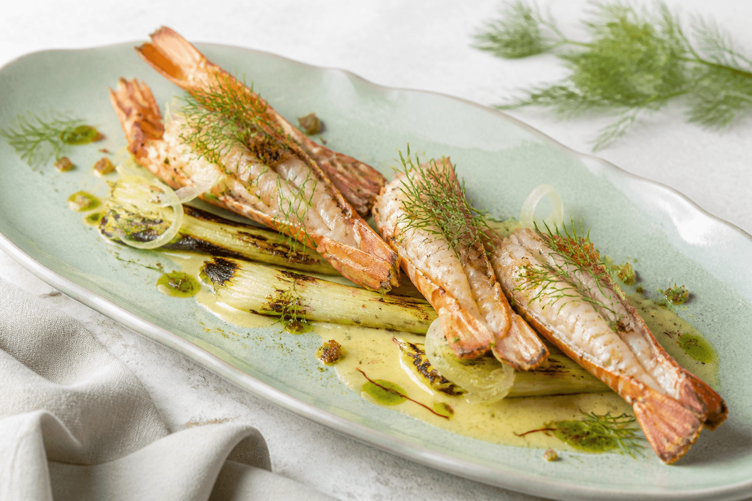 Smørgrillede jomfruhummerhaler med safran-beurre blanc, grillede små porrer, syltet fennikel, dildolie og rugknas på havgrønt fad