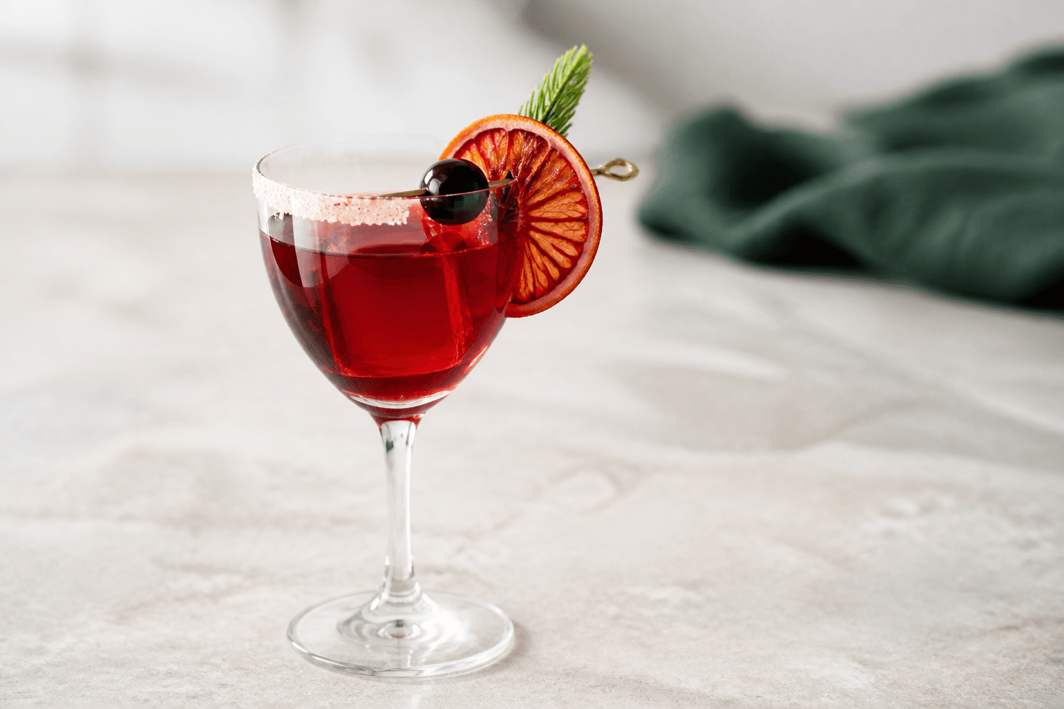 Klar dybrød kirsebær-blodappelsincocktail med rye whisky, kardemomme, tørret appelsin, amarena-kirsebær og granspids i stilkglas