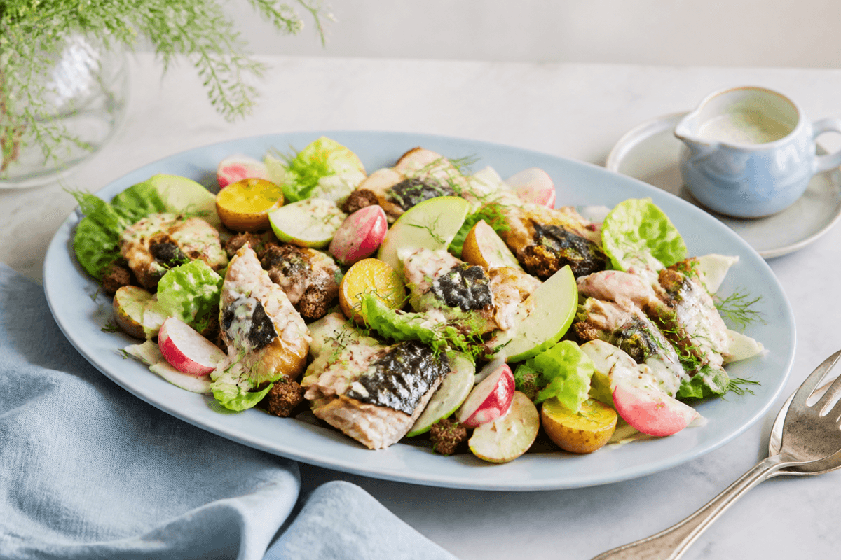 Stort lyseblåt ovalt fad med røget makrel, lune nye kartofler, fennikel, radiser, grønt æble, salat, rugcroutoner og kærnemælks-sennepsdressing