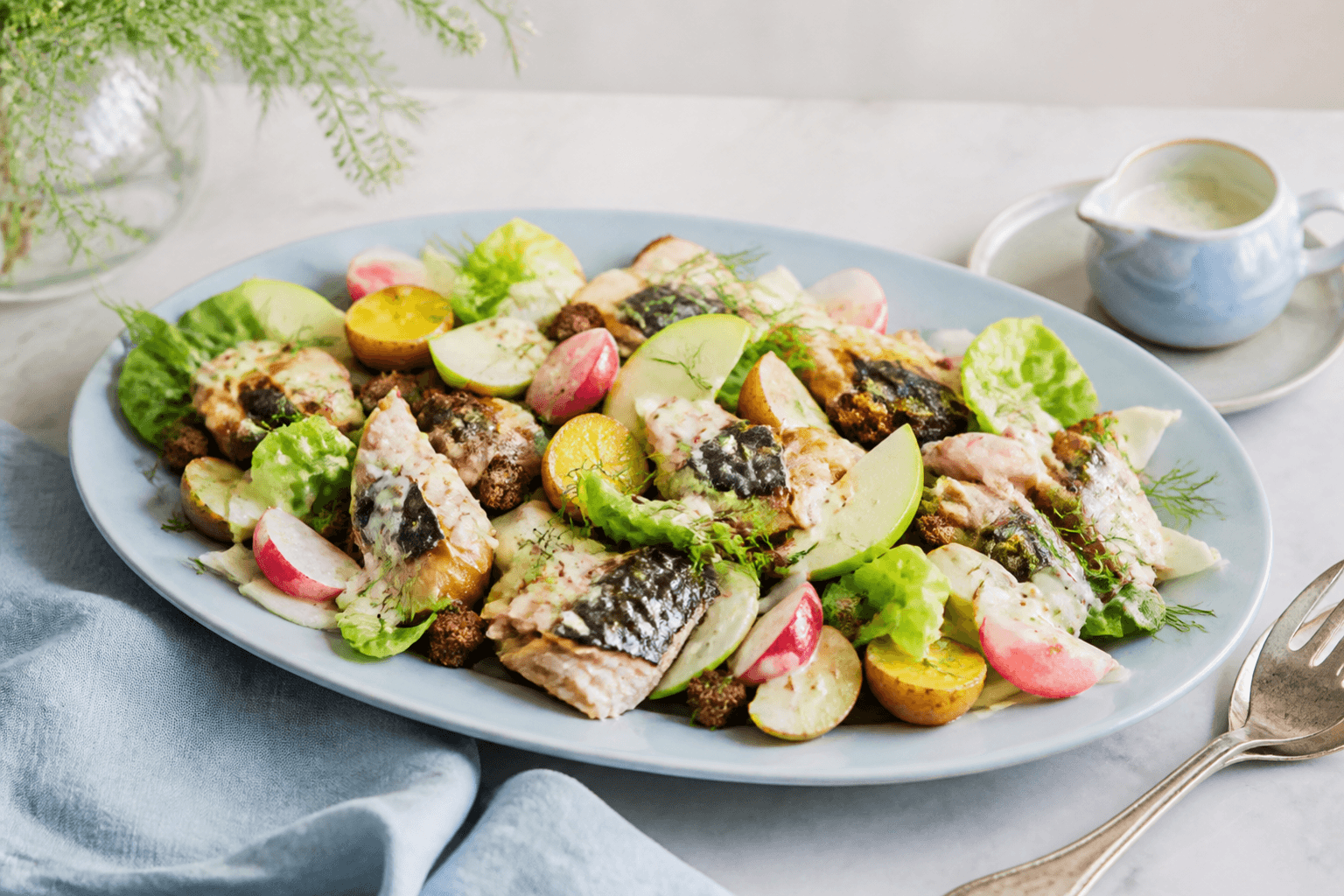 Stort lyseblåt ovalt fad med røget makrel, lune nye kartofler, fennikel, radiser, grønt æble, salat, rugcroutoner og kærnemælks-sennepsdressing