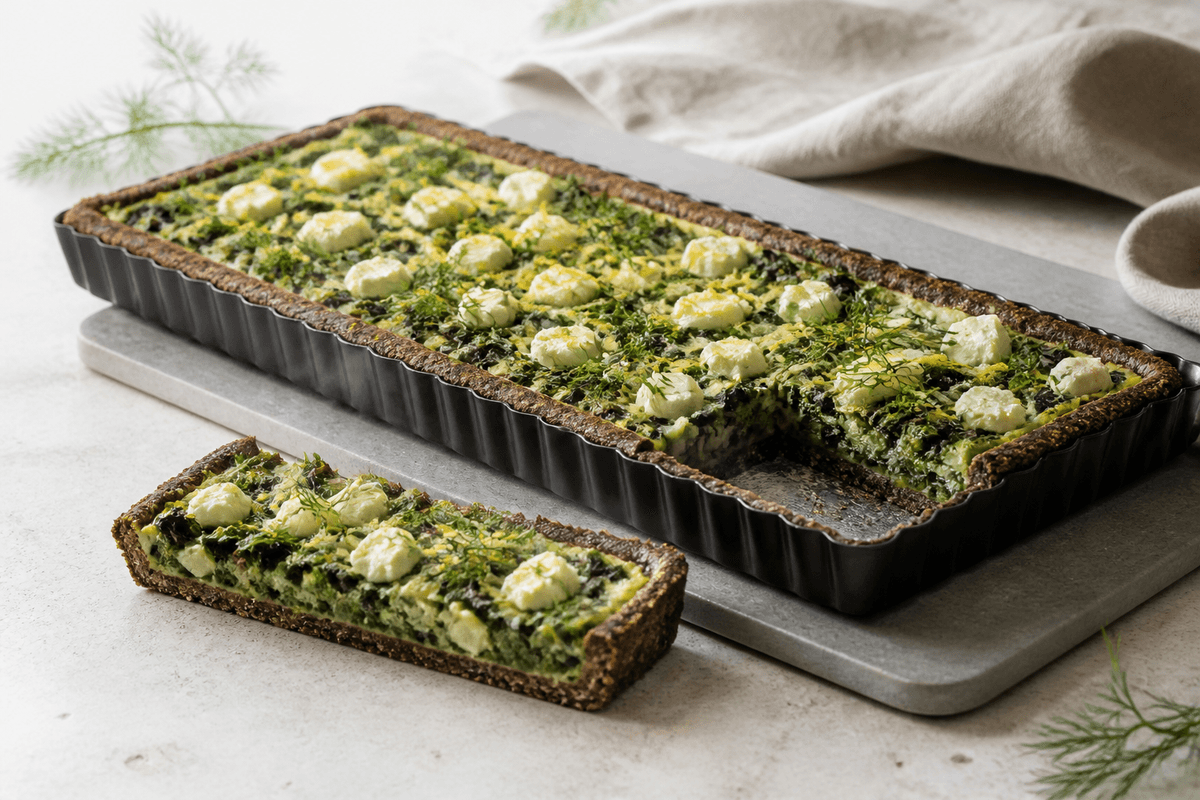 Lang rektangulær spinattærte med mørk rug-kartoffelbund, porre, feta, dild og citron i mat sort tærteform