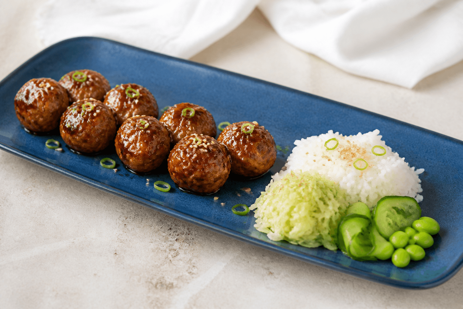 Otte blanke sesam-kyllingeboller med miso-appelsinglaze, jasminris, ingefærkål, agurk og edamame på langt blåt fad