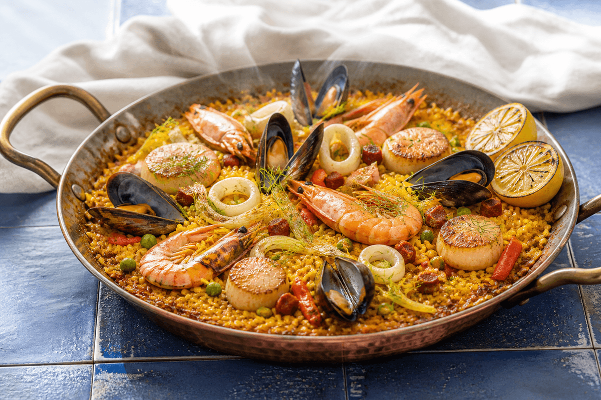 Safrangylden skaldyrspaella i hamret kobberpande med rejer, chorizo, åbne blåmuslinger, blæksprutteringe, stegte kammuslinger, fennikel og grillet citron