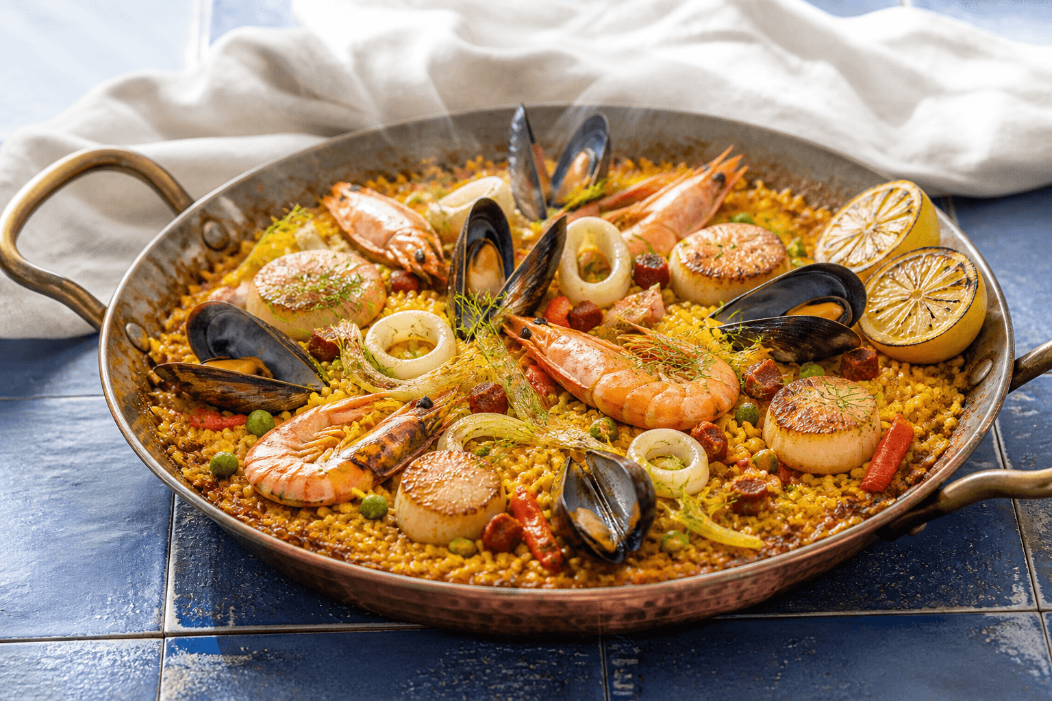 Safrangylden skaldyrspaella i hamret kobberpande med rejer, chorizo, åbne blåmuslinger, blæksprutteringe, stegte kammuslinger, fennikel og grillet citron