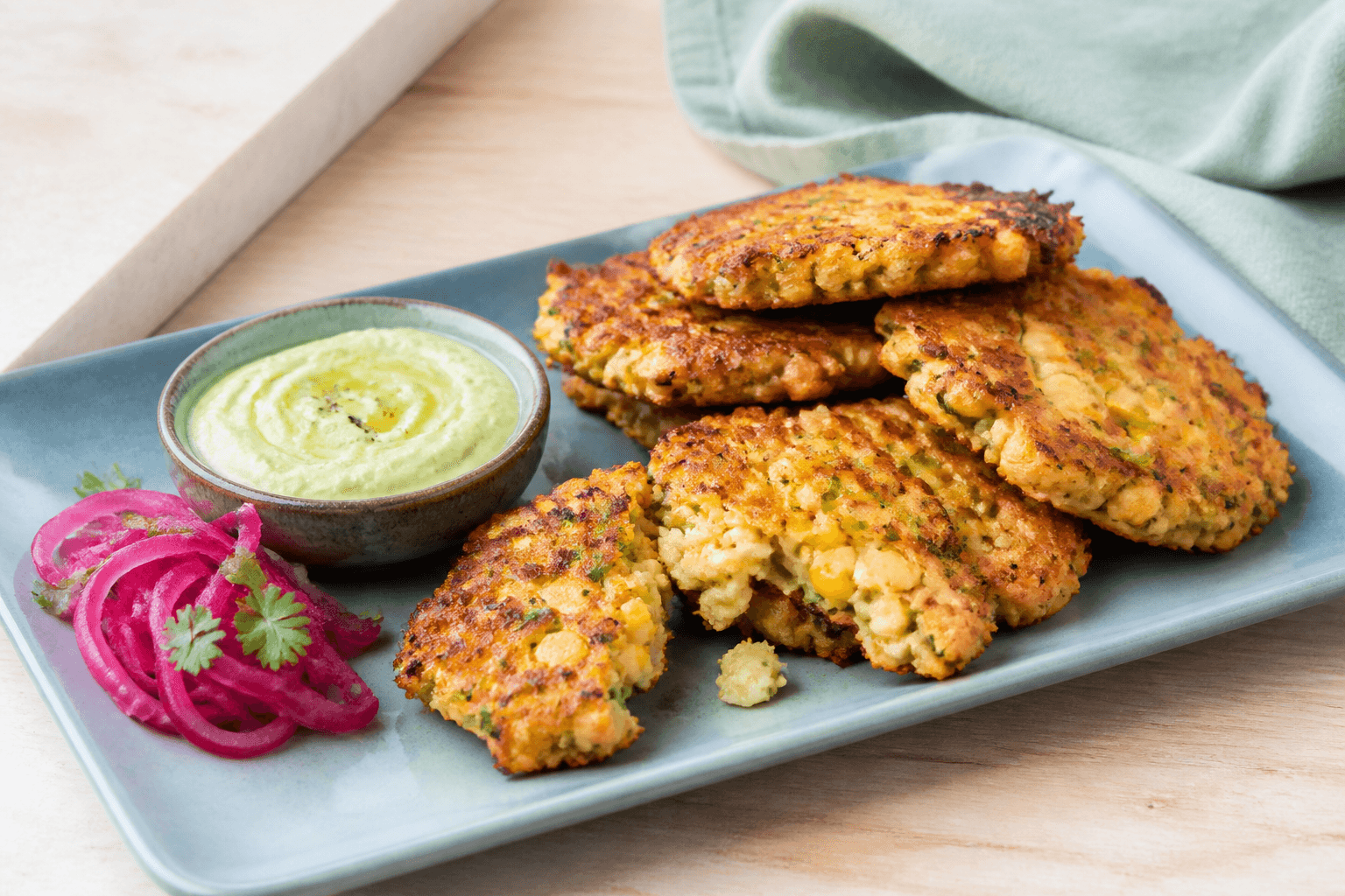 Tynde gyldne majsdeller med kikærter, halloumi, forårsløg og jalapeño på støvet blåt fad med avocado-skyr og syltet rødløg