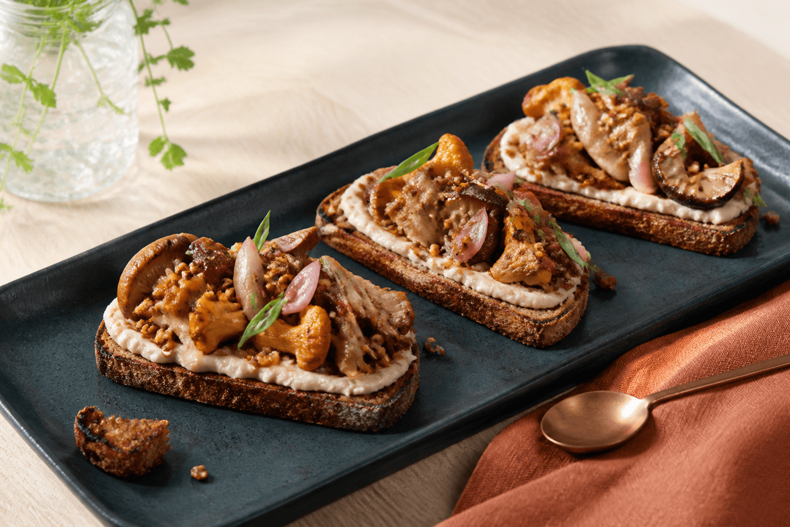 Tre grillede rugtoast med hvidbønnecreme, ristede skovsvampe, sherry-estragonfløde, syltede skalotteløg og sprød boghvede på mørkeblåt fad