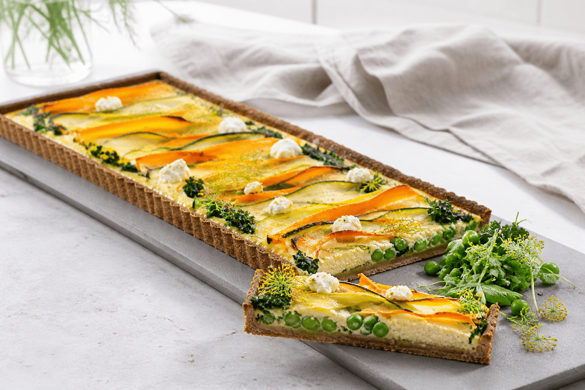 Lang grøntsagstærte med rugbund, bølgede gulerods- og squashbånd, porre, ærter, grønkål og citronricotta på gråt serveringsbræt