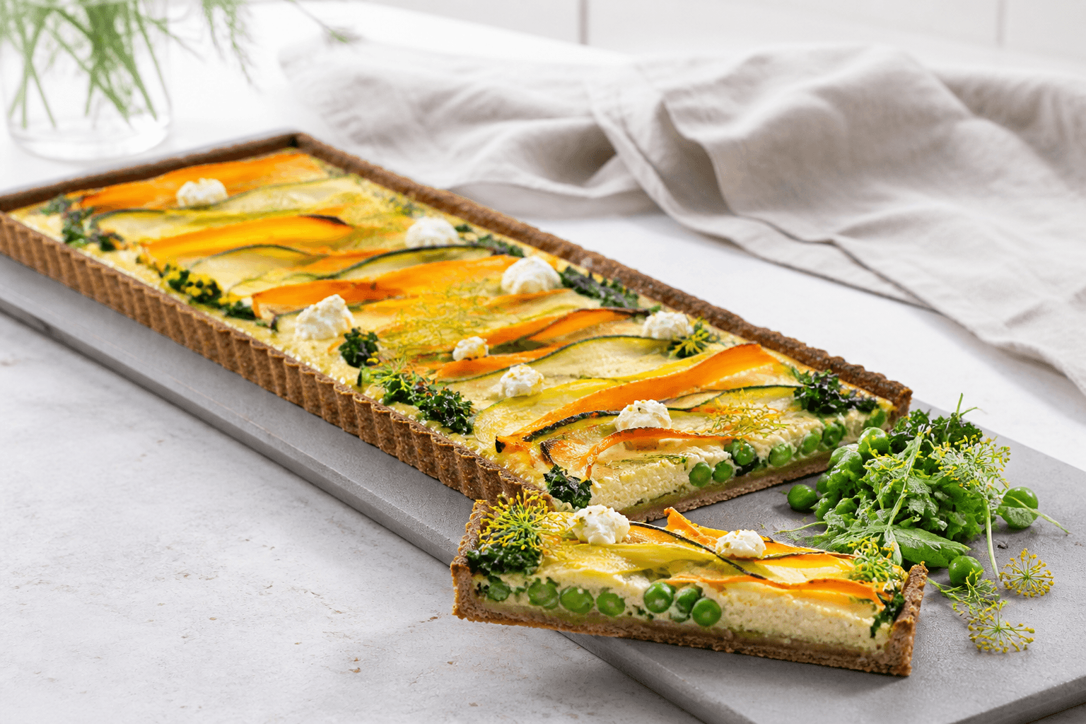 Lang grøntsagstærte med rugbund, bølgede gulerods- og squashbånd, porre, ærter, grønkål og citronricotta på gråt serveringsbræt