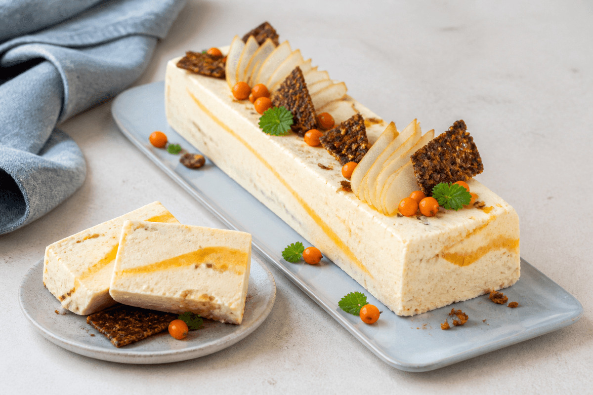 Aflang brunet smør-vaniljeparfait med orange havtornsripple, pocheret pære, rugkaramelskår og udskårne skiver på lyseblåt fad