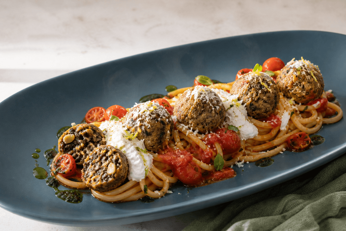 Spaghetti med sprøde beluga-aubergineboller, bagt tomatsauce, pisket ricotta, basilikumolie og citron-parmesan på et langt petrolblåt fad