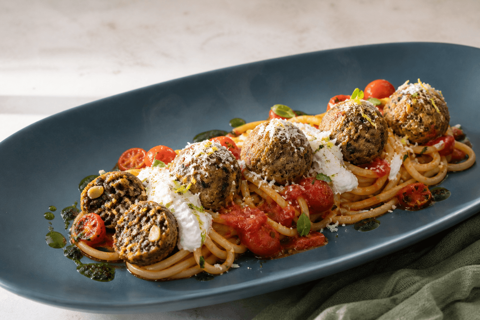 Spaghetti med sprøde beluga-aubergineboller, bagt tomatsauce, pisket ricotta, basilikumolie og citron-parmesan på et langt petrolblåt fad