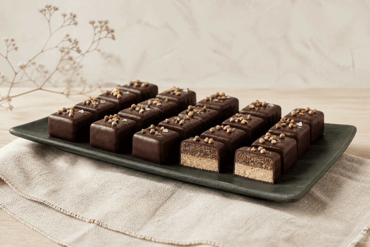 Lagdelte nougatpraliner med mørk chokolade, hasselnøddepraline og saltet rugkaramel på et mørkegrønt fad