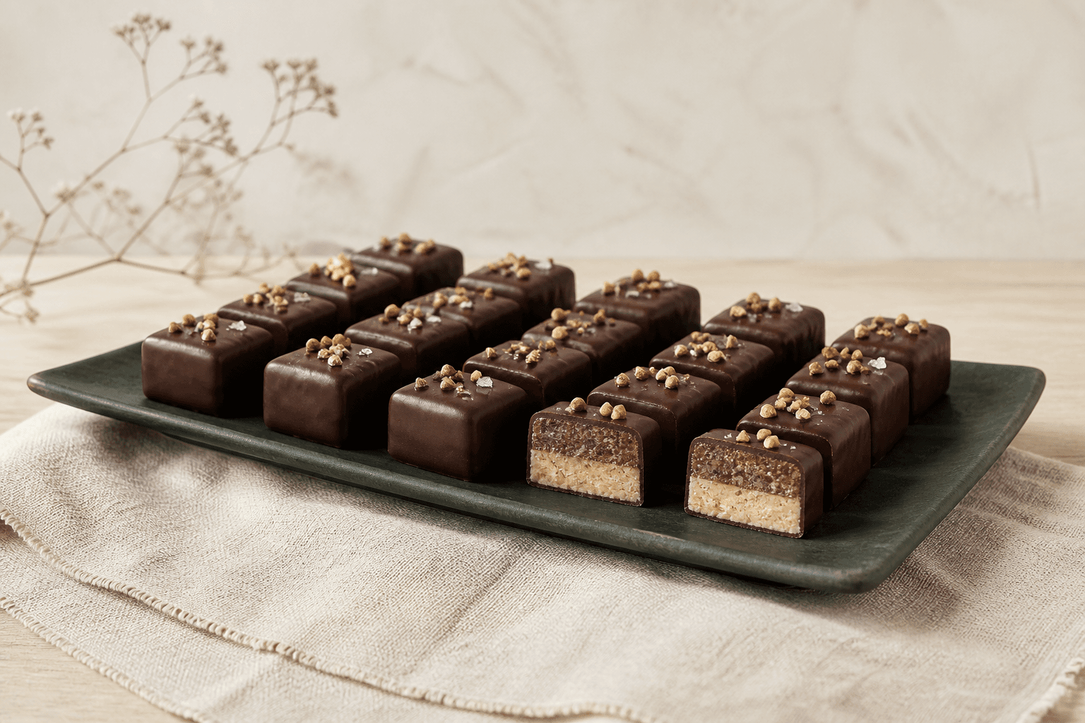 Lagdelte nougatpraliner med mørk chokolade, hasselnøddepraline og saltet rugkaramel på et mørkegrønt fad